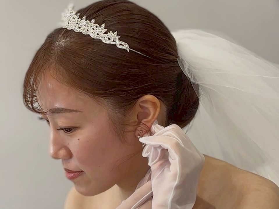 新横浜の結婚式場でのお支度中の花嫁。ティアラを着用し、白手袋で耳元を整える横顔のアップ。上品なシニヨンスタイル。