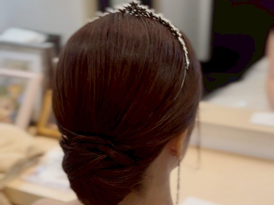 花嫁のバックスタイル。低めの位置で丁寧に編み込まれた艶のあるシニヨンヘアと、繊細なティアラのかさなり。
