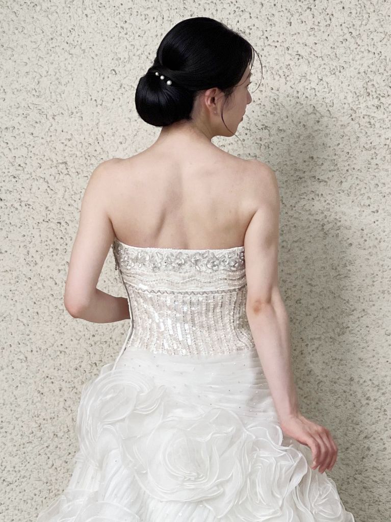 首から肩の沿うようなやや大きめのシニヨンで落ち着いたイメージ。髪飾りはパールでシンプルに仕上げました。