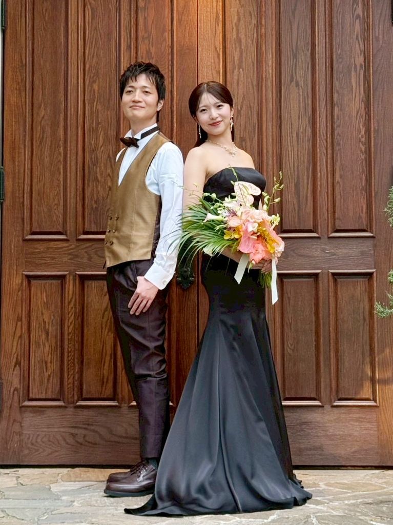 お色直し後の新郎新婦。新婦は黒いドレス、新郎はベストスタイルで、ブーケを手にポーズをとる。